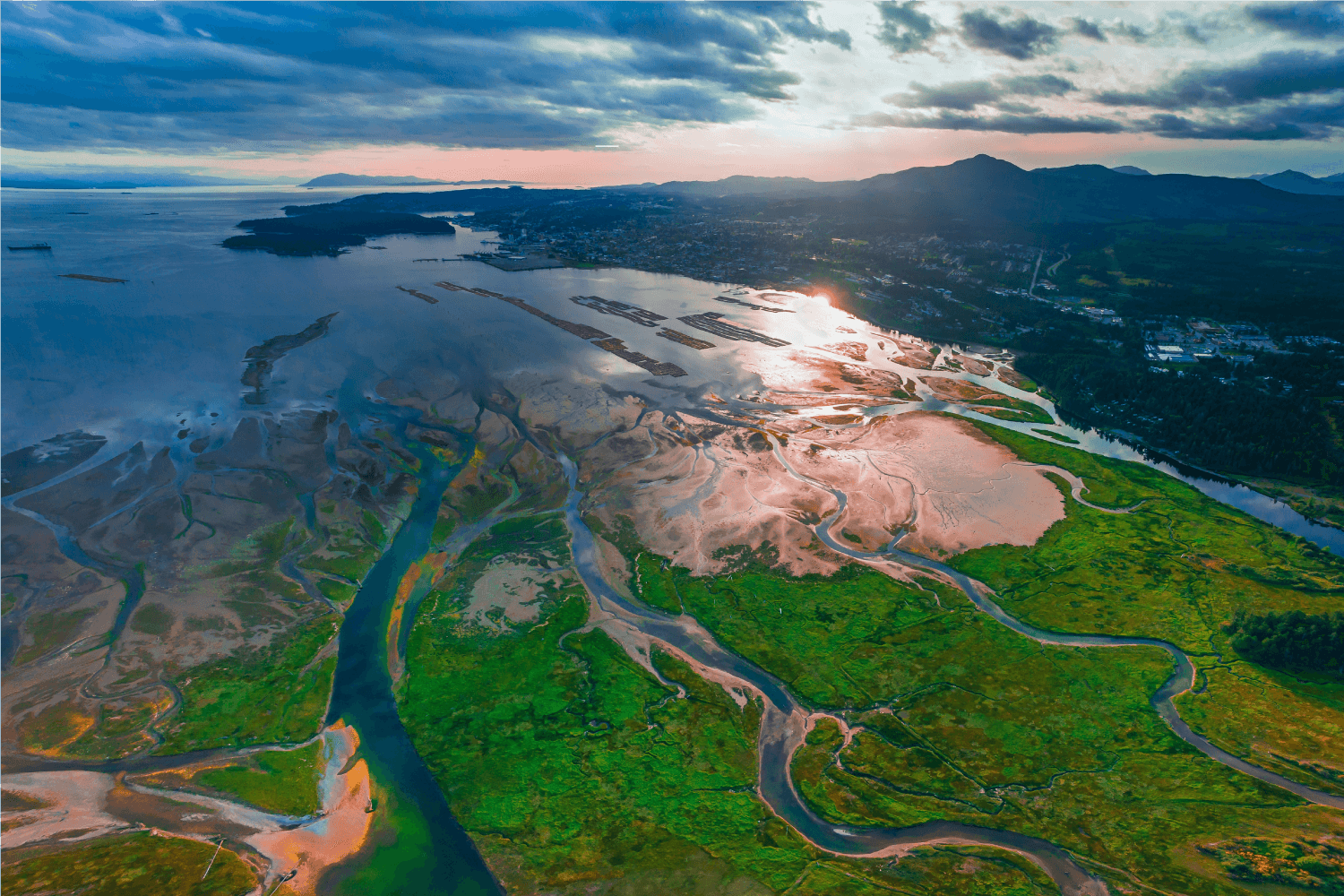 Aerial view of a river joining the ocean at sunset with mountains in the background