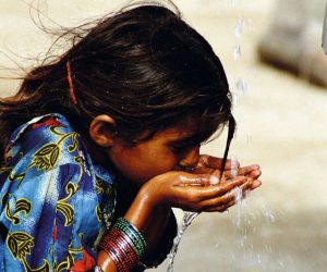 Young indian woman drinking water with her hands underneath a water stream
