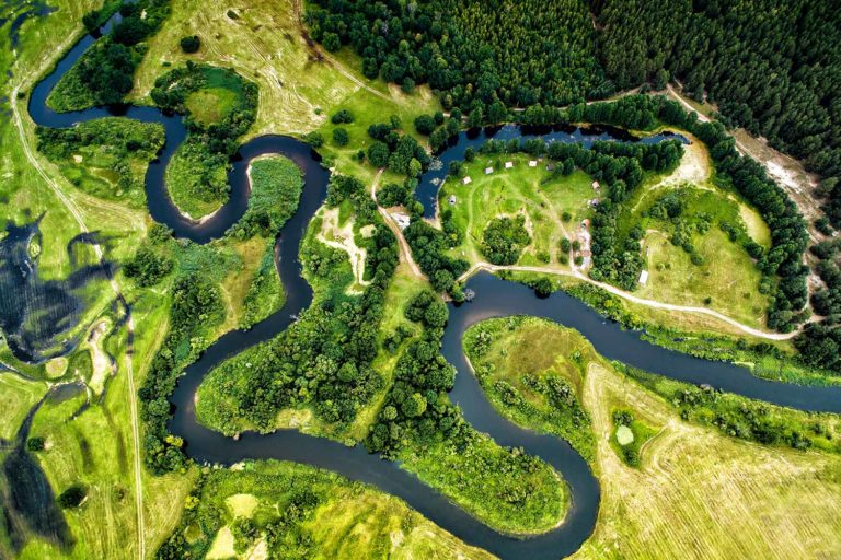 Aerial view of a meandering river between green fields and forests.