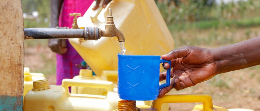 Hand holding a cup below a flowing water tap