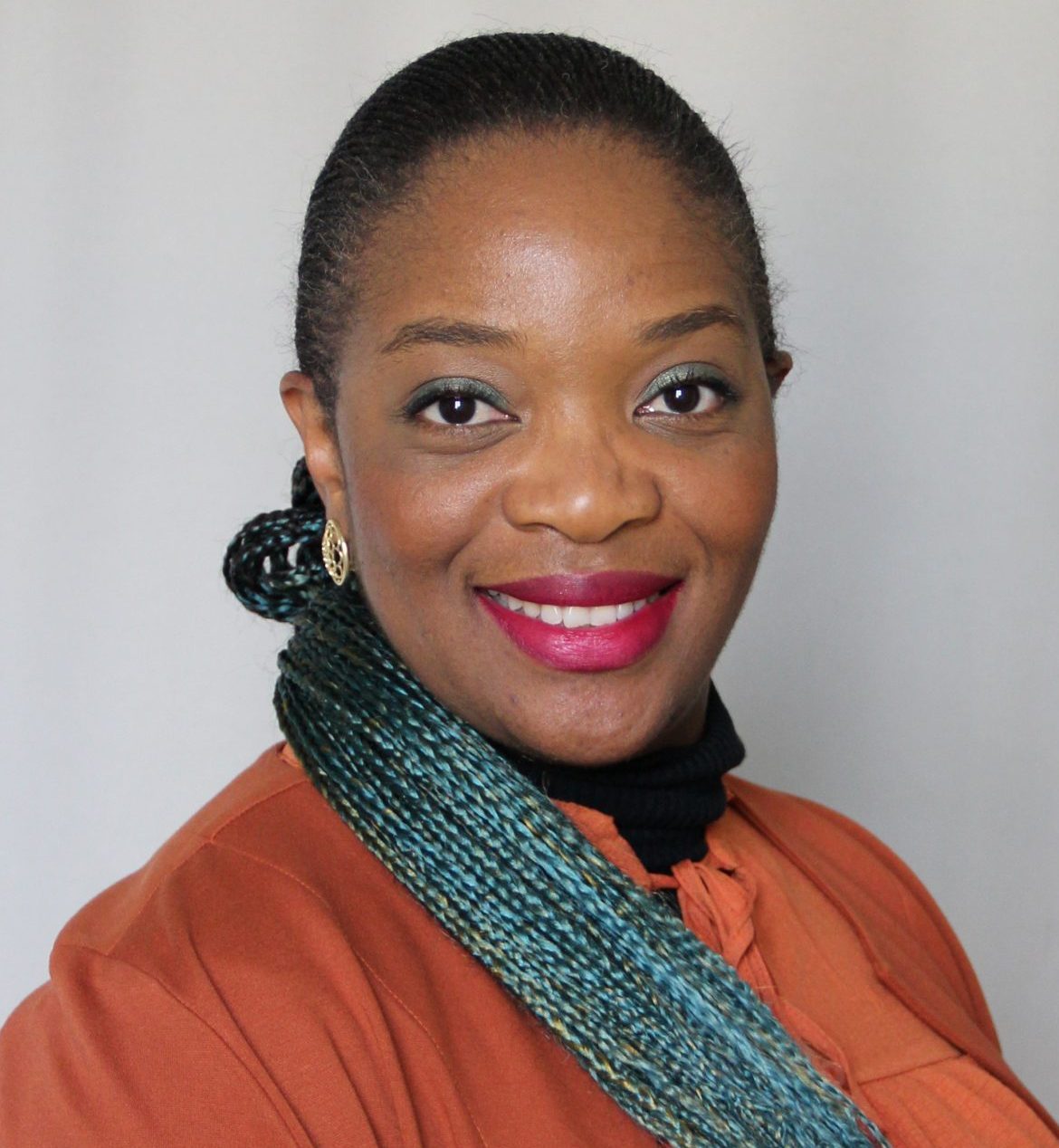 Woman in orange shirt with bright blue braids and pink lipstick with a broad smile