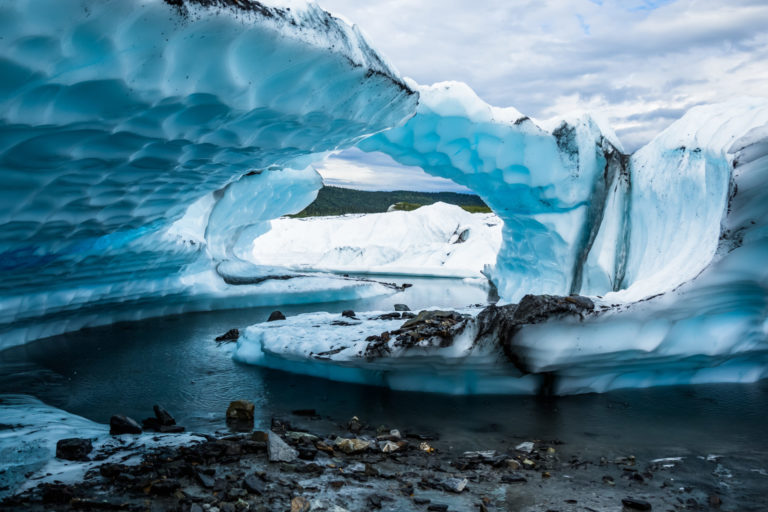 A narrow, winding river of meltwater on the Matanuska Glacier carved several large fins of overhanging ice. The layers of fins Appear to form an arch from the side.