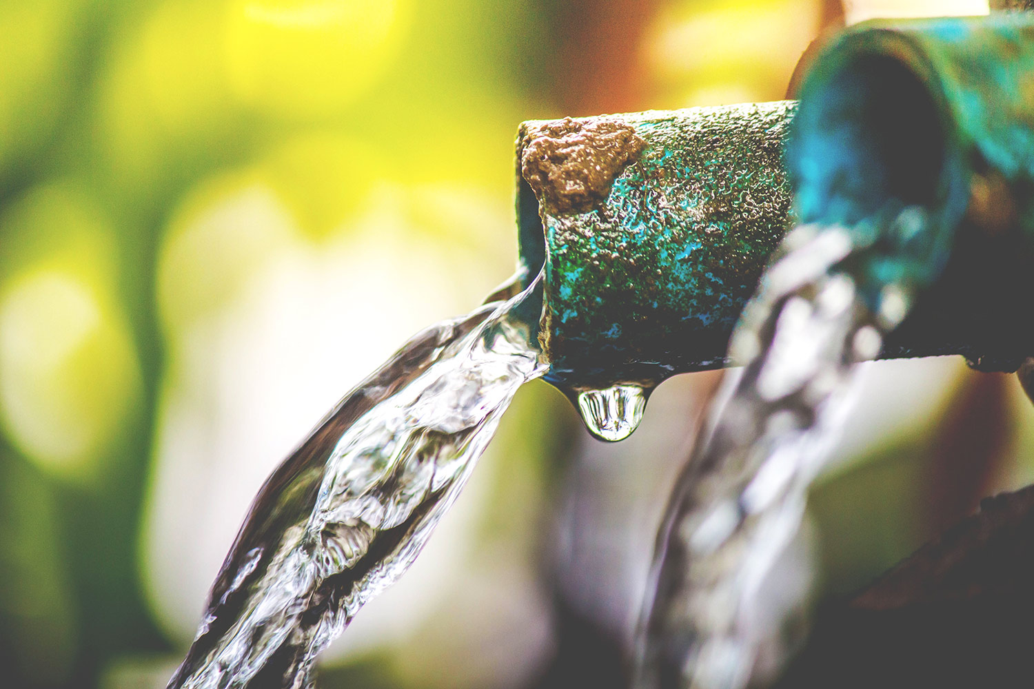 Water going out of rusty taps on blurry green forest background