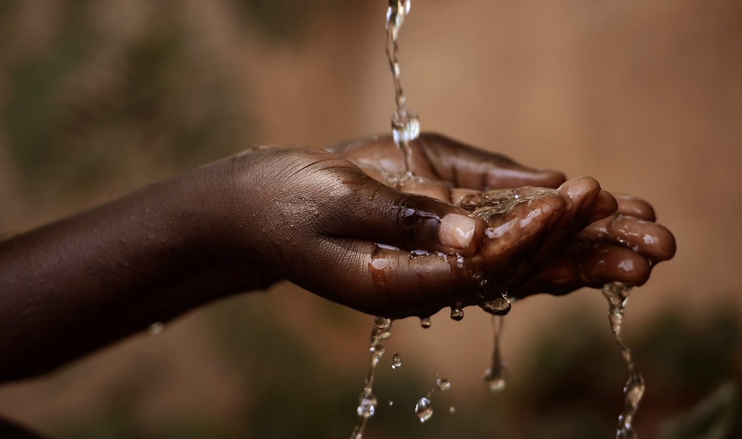 Hands of a young black person receiving water under a thin water stream