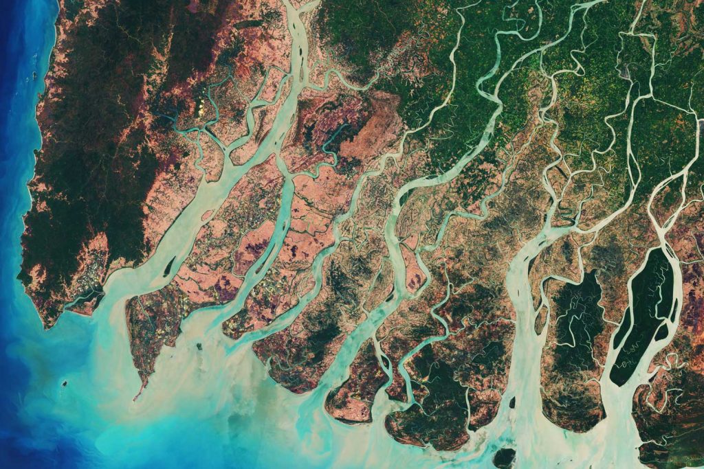 Aerial view of a river delta: the green water from the river mixes into the blue ocean