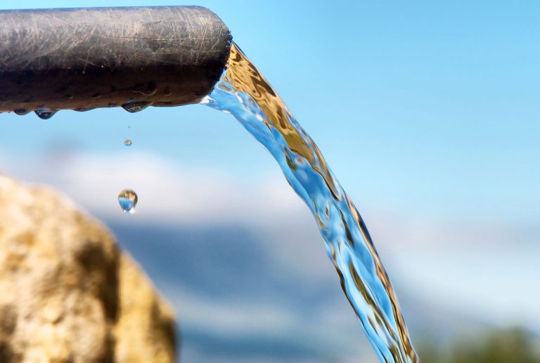 Water going out of a pipe on blurry mountain background, in South Africa