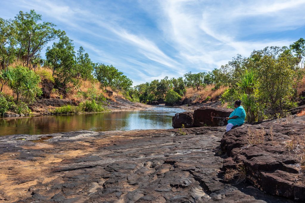 Mitchell Plateau, WA, Australia - May31, 2015: An indigenous Australian woman from the local Kandiwal community sits beside a prisitne outback river. (Photo: Philip Schubert)