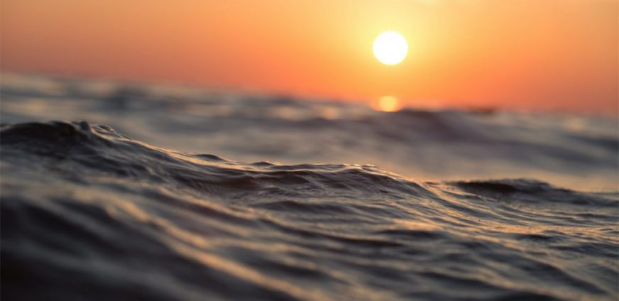 wavy surface of a water body at sunset with an orange sky
