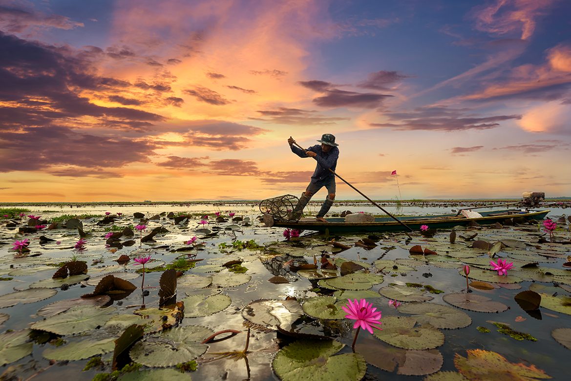 Fisherman boating using crutches for fishing in sea pink lotus of sunrise