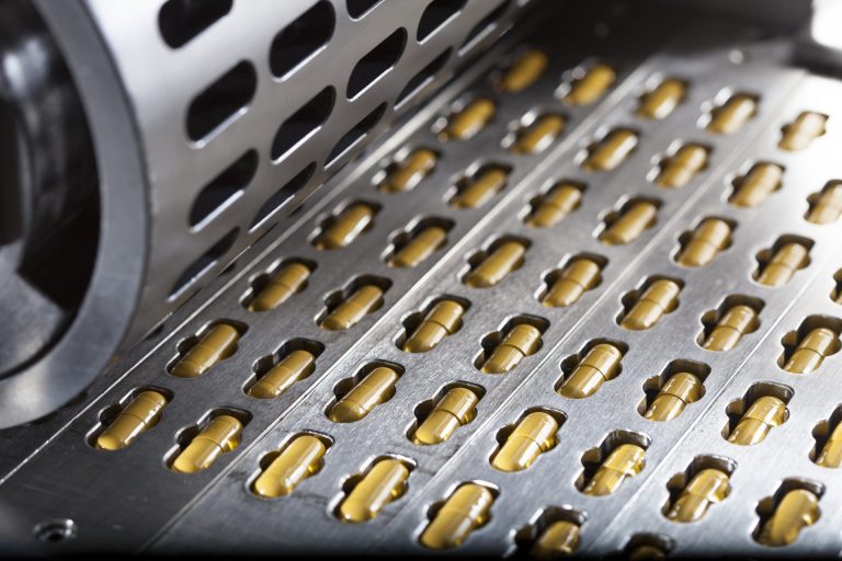 Lines of yellow pills arranged in slots on a production machine