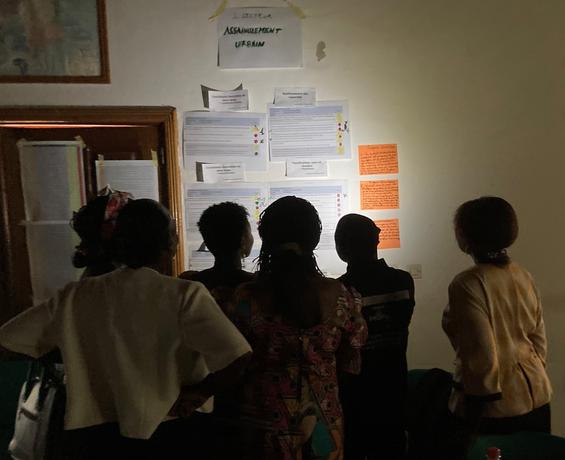 Participants, with their backs facing the camera, at a workshop on water, sanitation and hygiene read notes pasted to a wall in Central African Republic.
