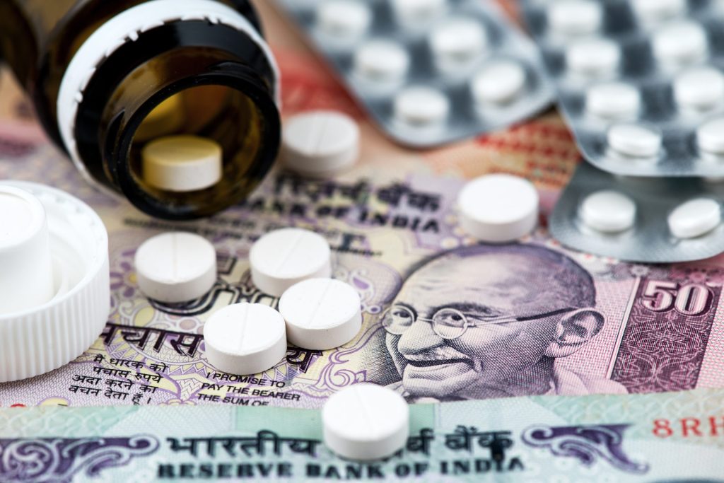 White circular pills over Indian currency notes scattered from a dark glass bottle