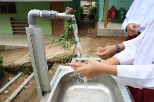 A child's hands under a tap of water over a sink, in an outdoors setting resembling a school