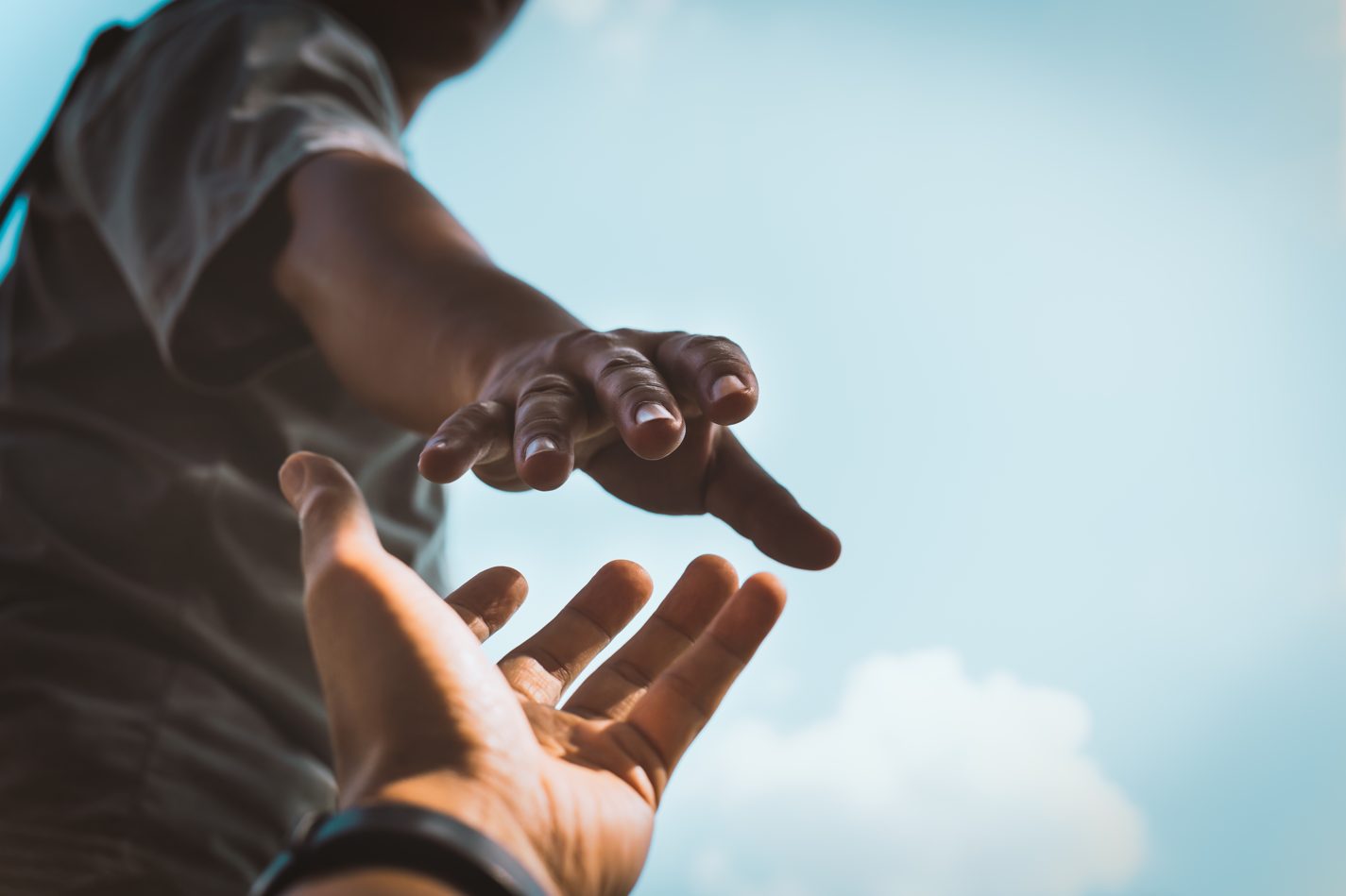 2 hands of young people reaching to each other on a cloudy background