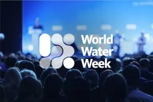 Crowd seen from the back with people speaking on stage, blurred in the background. World Water Week 
