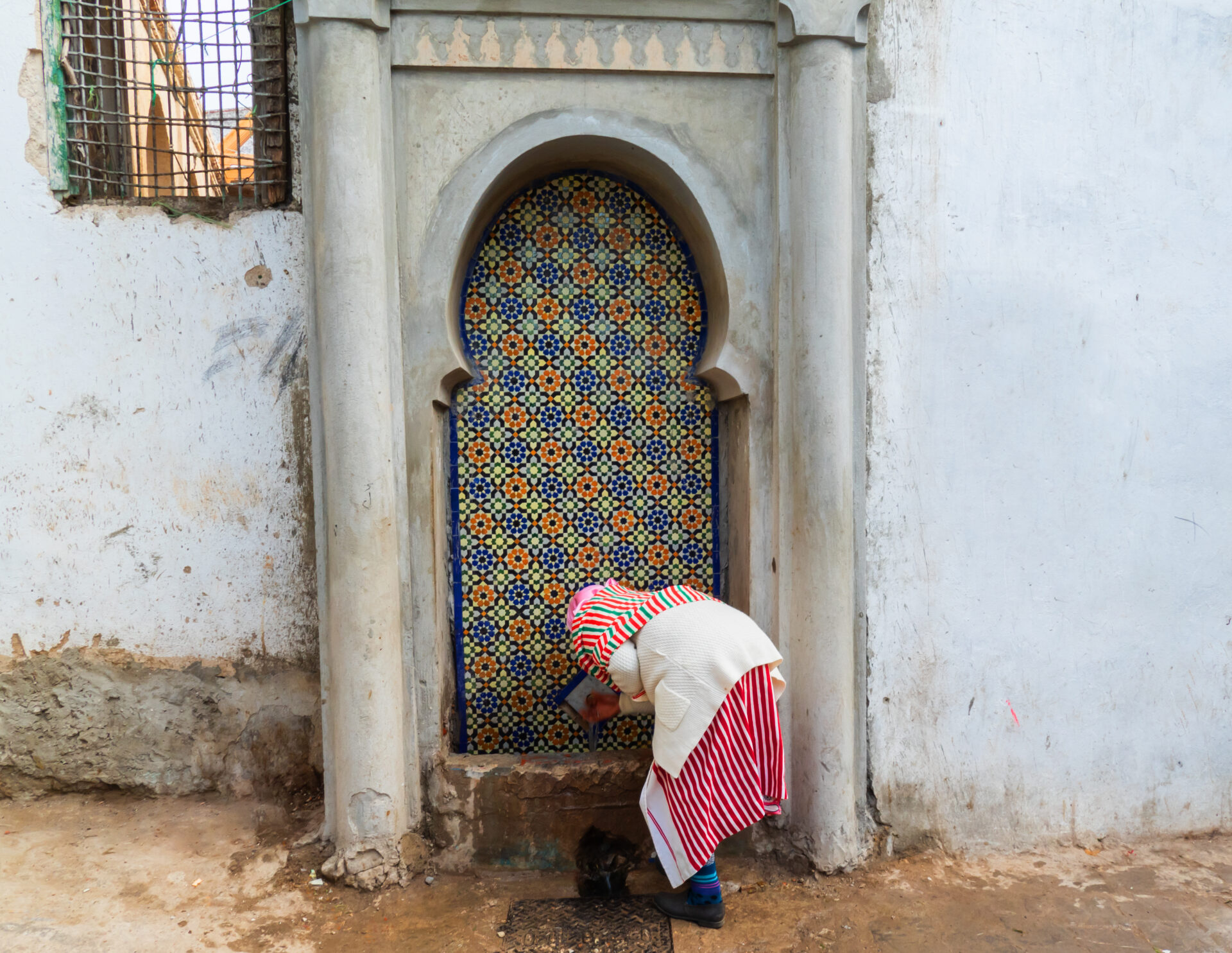 Woman drinking from a traditional fountain in Tetouan, Morocco