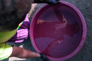 Picture of a young person holding onto and looking into a maroon bucket but only the reflection is visible