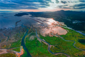 Aerial view of a river joining the ocean at sunset with mountains in the background