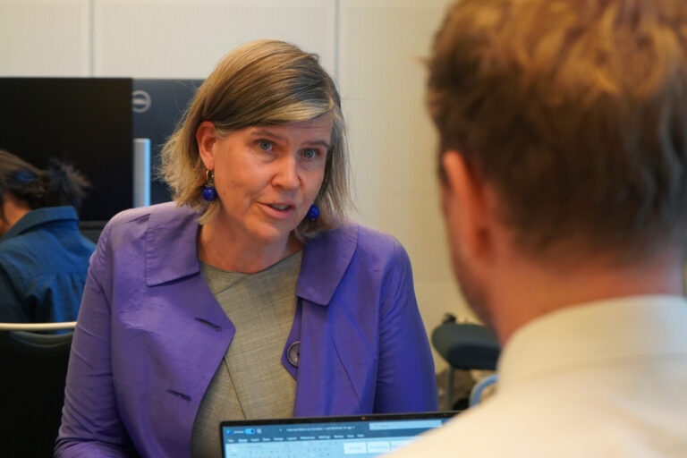 Meike van Ginneken sitting, facing the camera, in front of Jakob Schabus (from the back). She is wearing a purple jacket and a light grey top.